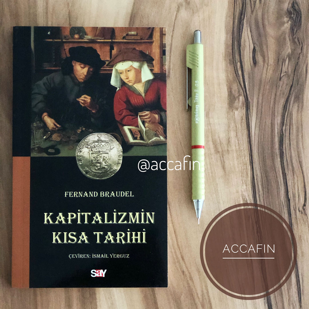 Fernand Braudel'in Kapitalizmin Kısa Tarihi kitabı (Say Yayınları, çeviren İsmail Yerguz) ahşap masada, yanında kalem ve accafin rozeti