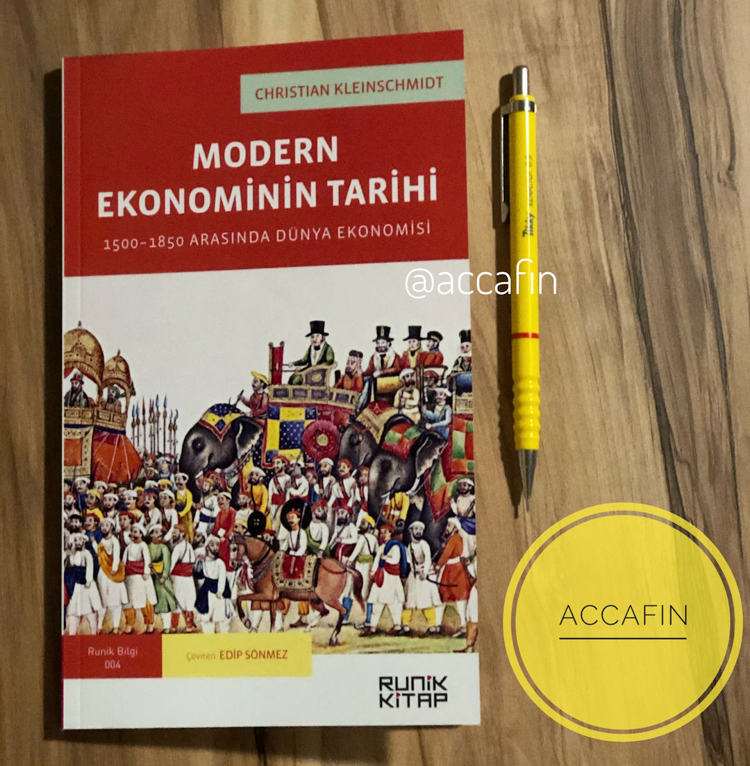 Christian Kleinschmidt'in Modern Ekonominin Tarihi: 1500–1850 Arasında Dünya Ekonomisi kitabı (Runik Kitap, çeviren Edip Sönmez) ahşap masada, yanında kalem ve accafin rozeti