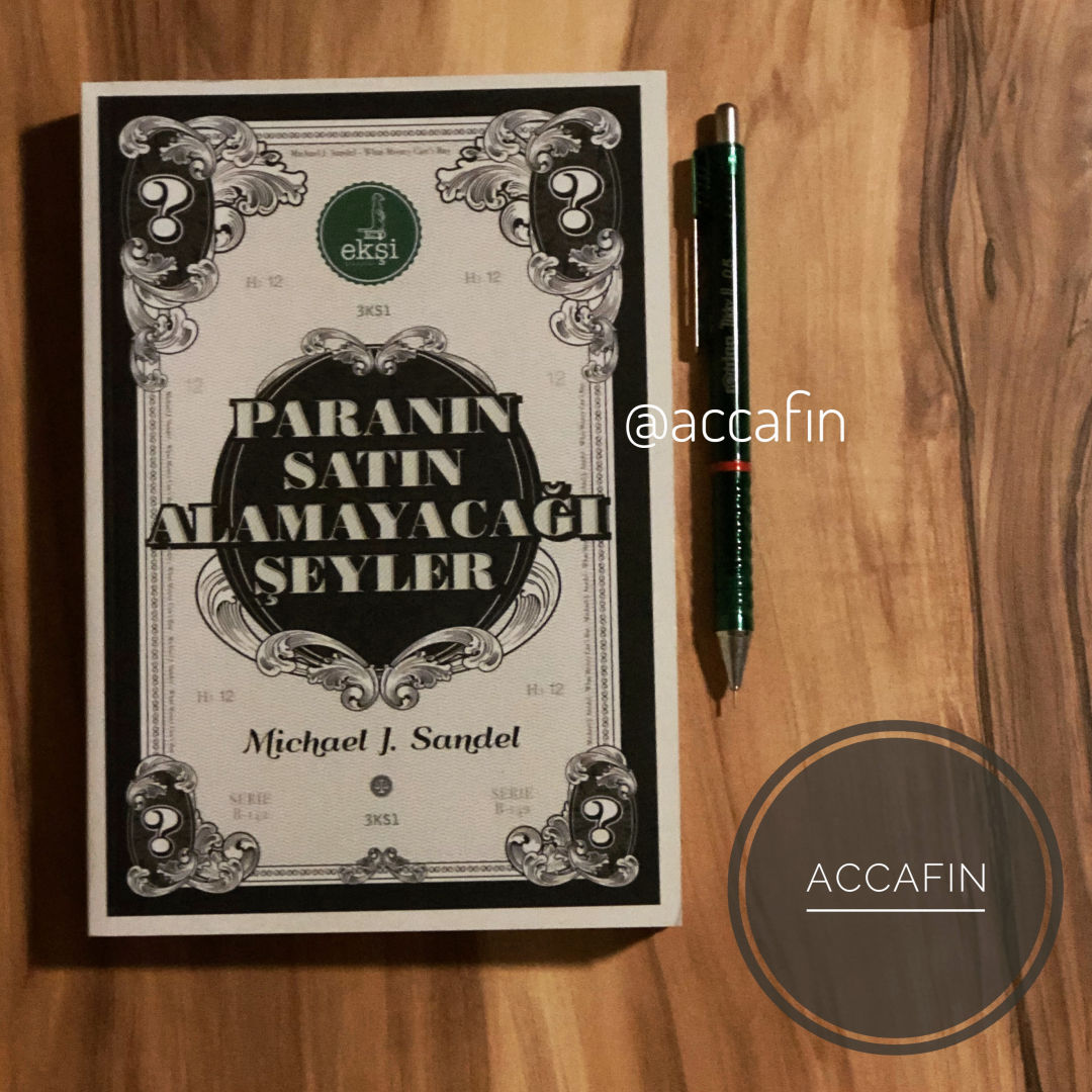 Michael J. Sandel'in Paranın Satın Alamayacağı Şeyler kitabı ahşap masada, yanında kalem ve accafin rozeti