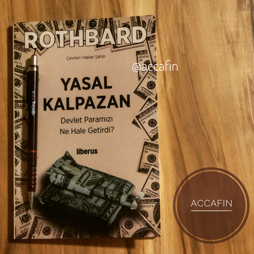 Murray Rothbard'ın Yasal Kalpazan: Devlet Paramızı Ne Hale Getirdi? kitabı (Liberus, çeviren Hakan Şahin) ahşap masada, yanında kalem ve accafin rozeti